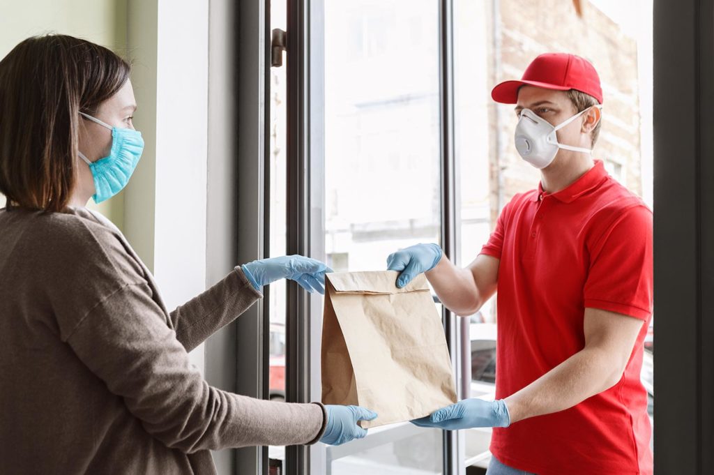 Delivery driver handing over food in paper bag whilst wearing mask and gloves