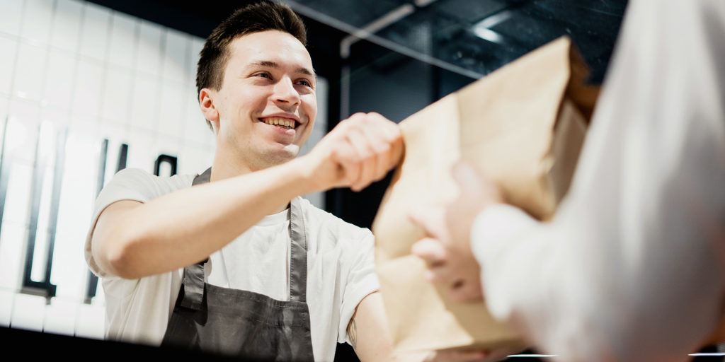 Young male employee handing over takeaway food in paper bag